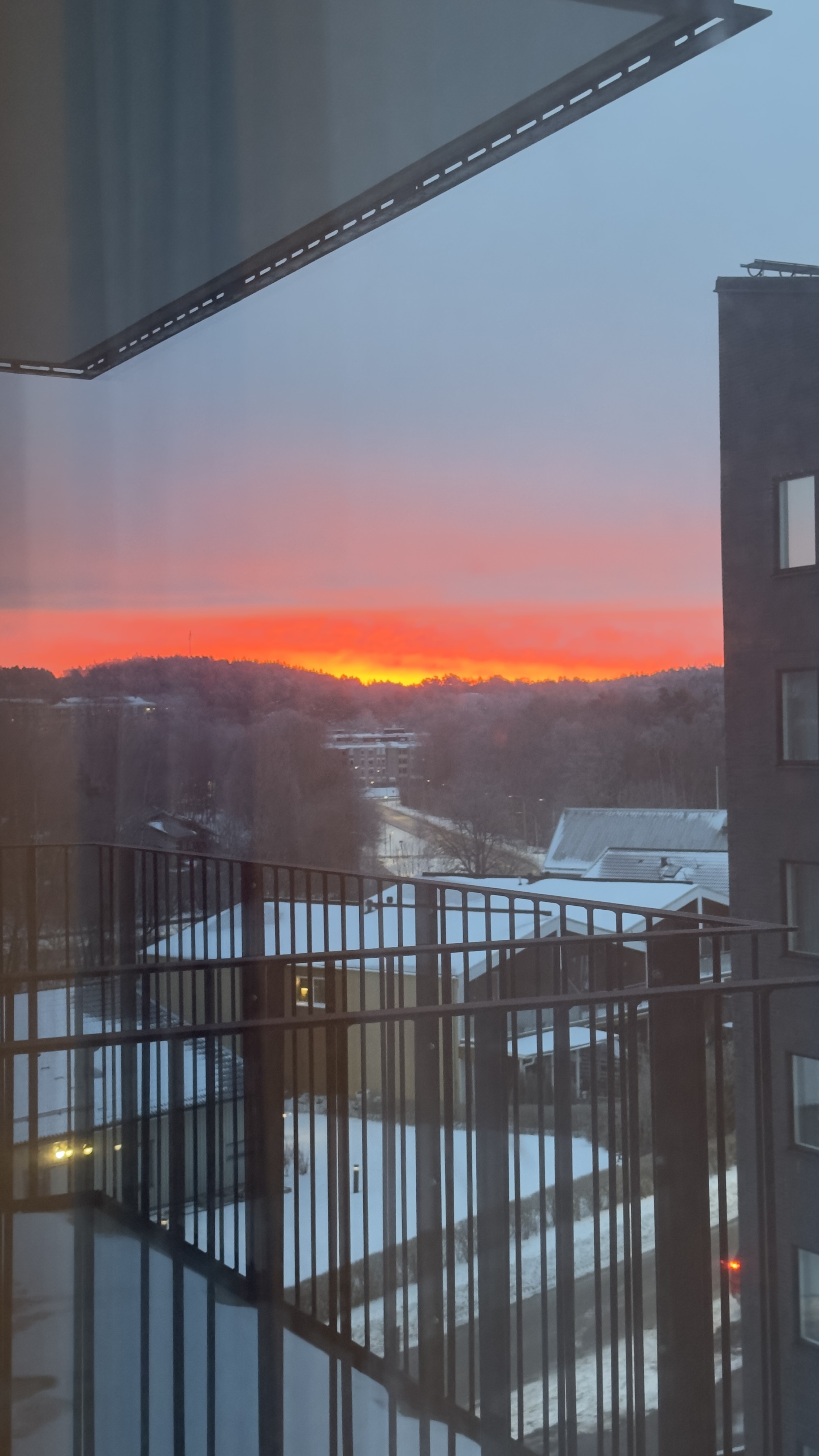 An orange sunset over snowy buildings, seen from a balcony